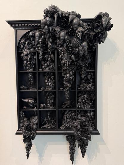 Another black wall cabinet filled and encrusted with shells and other items, all painted black.