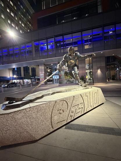 Base of the statue is Tyndall stone.

Statue of Dale Hawerchuk, who, according to a plaque
"put the Winnipeg Jets Hockey Club on the map the day he arrived in our city in 1981, and his love for our community and remarkable Hall of Fame career will keep it there for many generations to come.
Our players, alumni and fans will forever be inspired by his passion for the game and his commitment to his team.
Bronze statue by Erik Blome,
inspired by a photograph by Bruce Bennett.
Dedicated October 2022