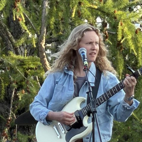 A person playing an electric guitar, looking off to their left 
