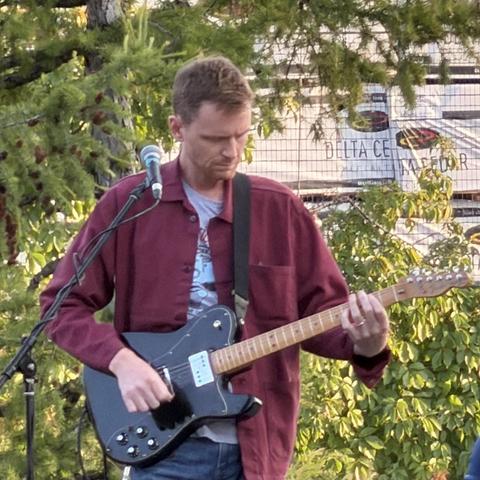 A person playing the electric guitar, looking down at their left hand on the frets
